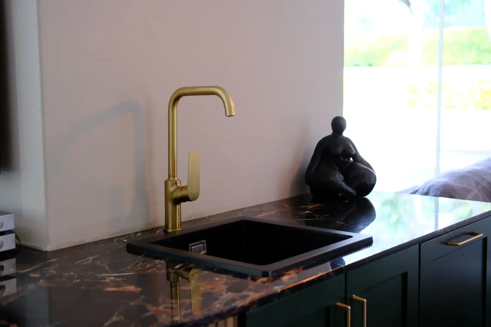 Brushed brass gooseneck kitchen mixer over a black sink on a dark marble benchtop