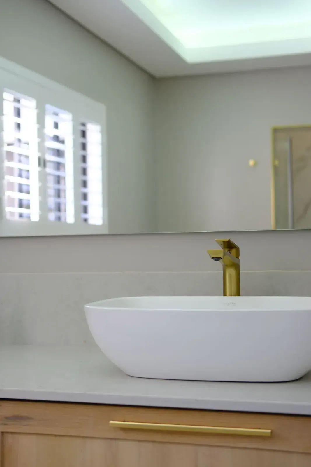 Brushed brass wall-mounted basin mixer in a bright bathroom