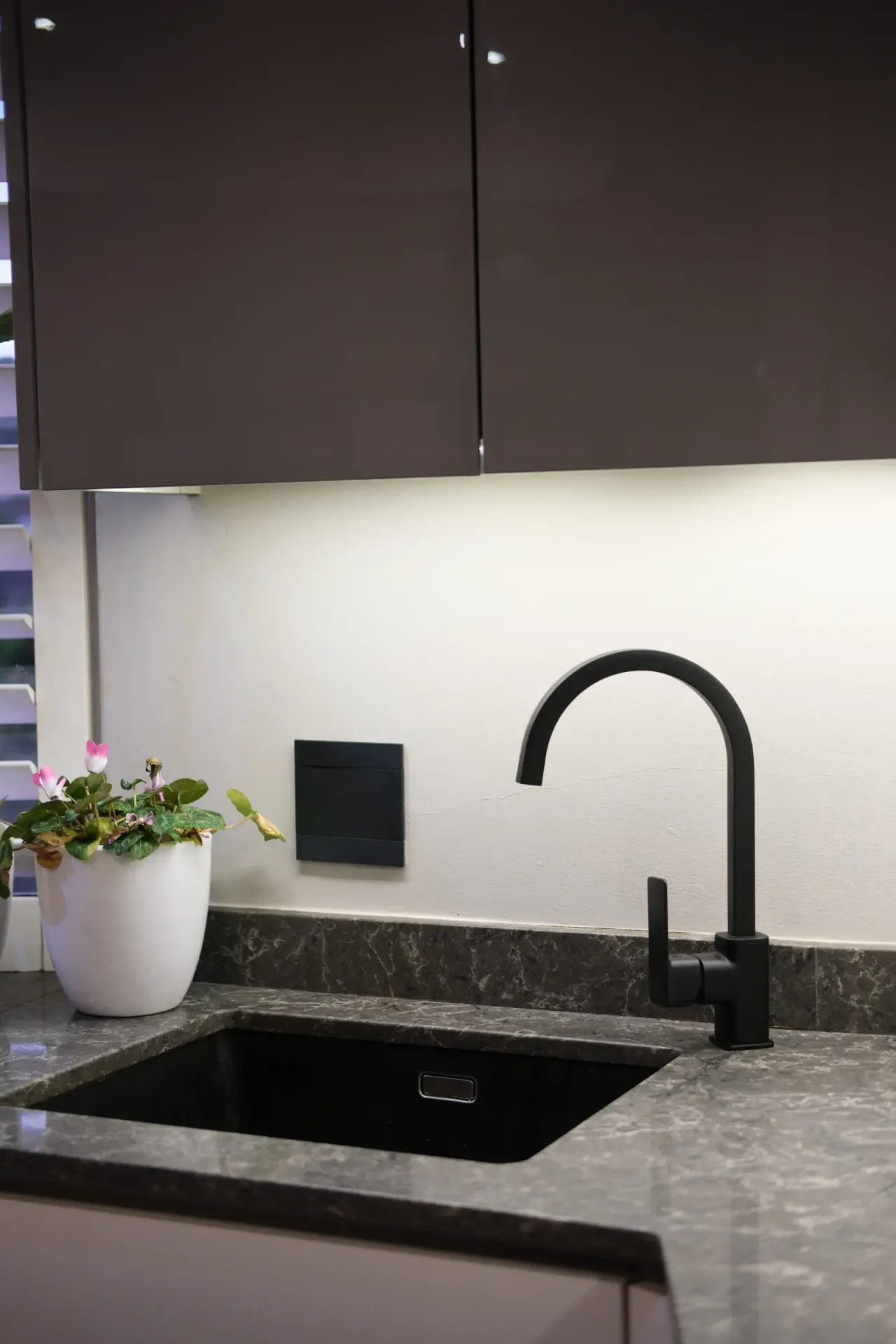 Matte black gooseneck kitchen mixer over a black undermount sink on a grey stone benchtop