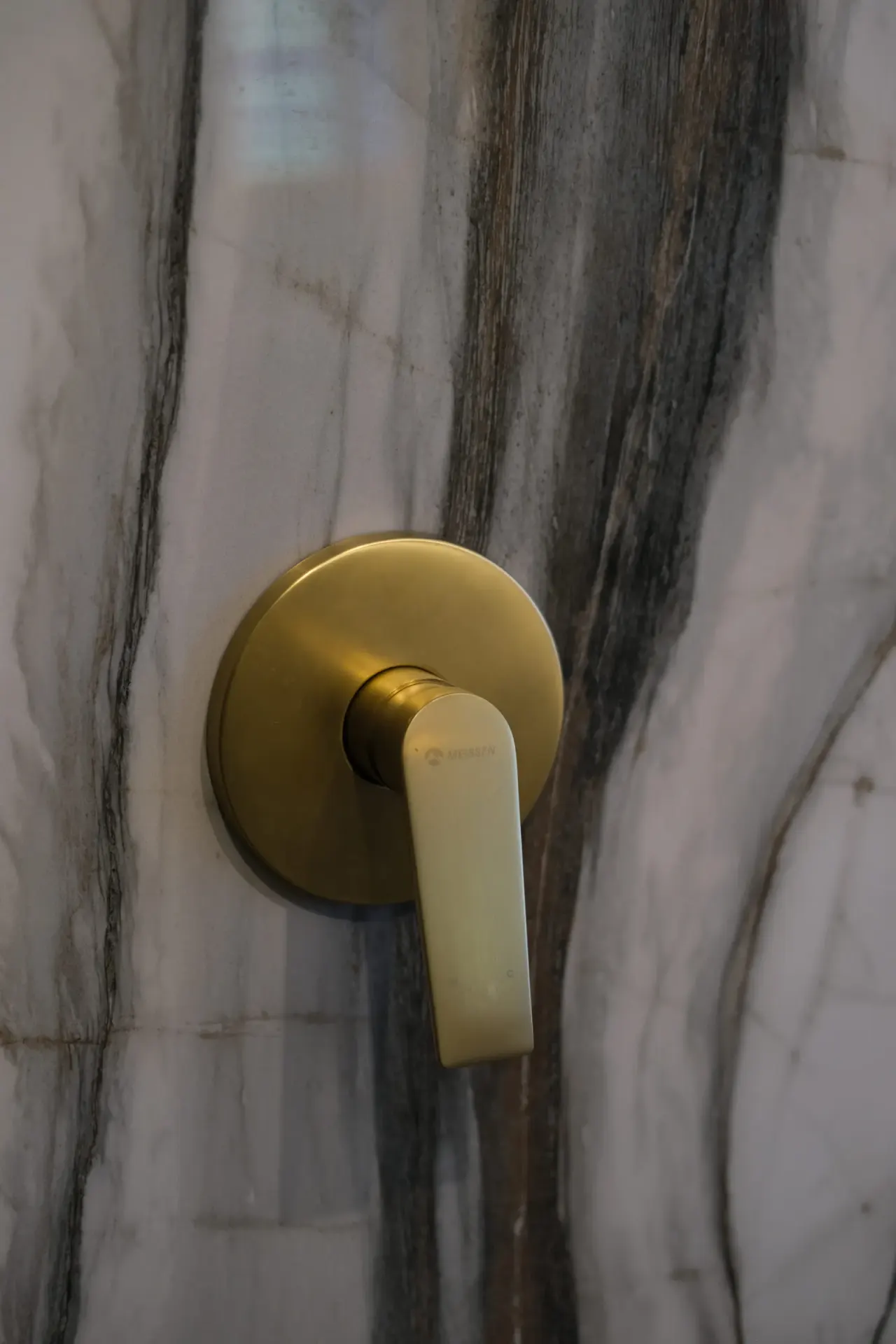 Brushed brass wall-mounted basin mixer on a marble wall