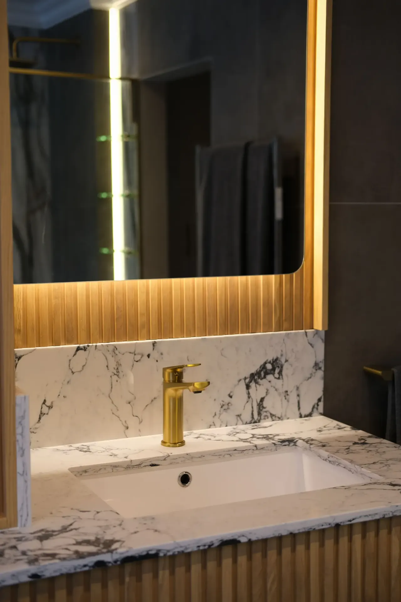 Brushed brass tall basin mixer on a marble vanity with a backlit mirror