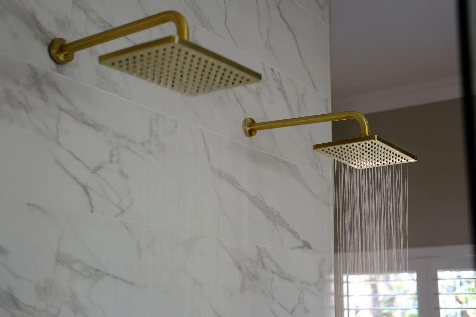 Brushed brass square rain shower heads running on a marble tiled wall