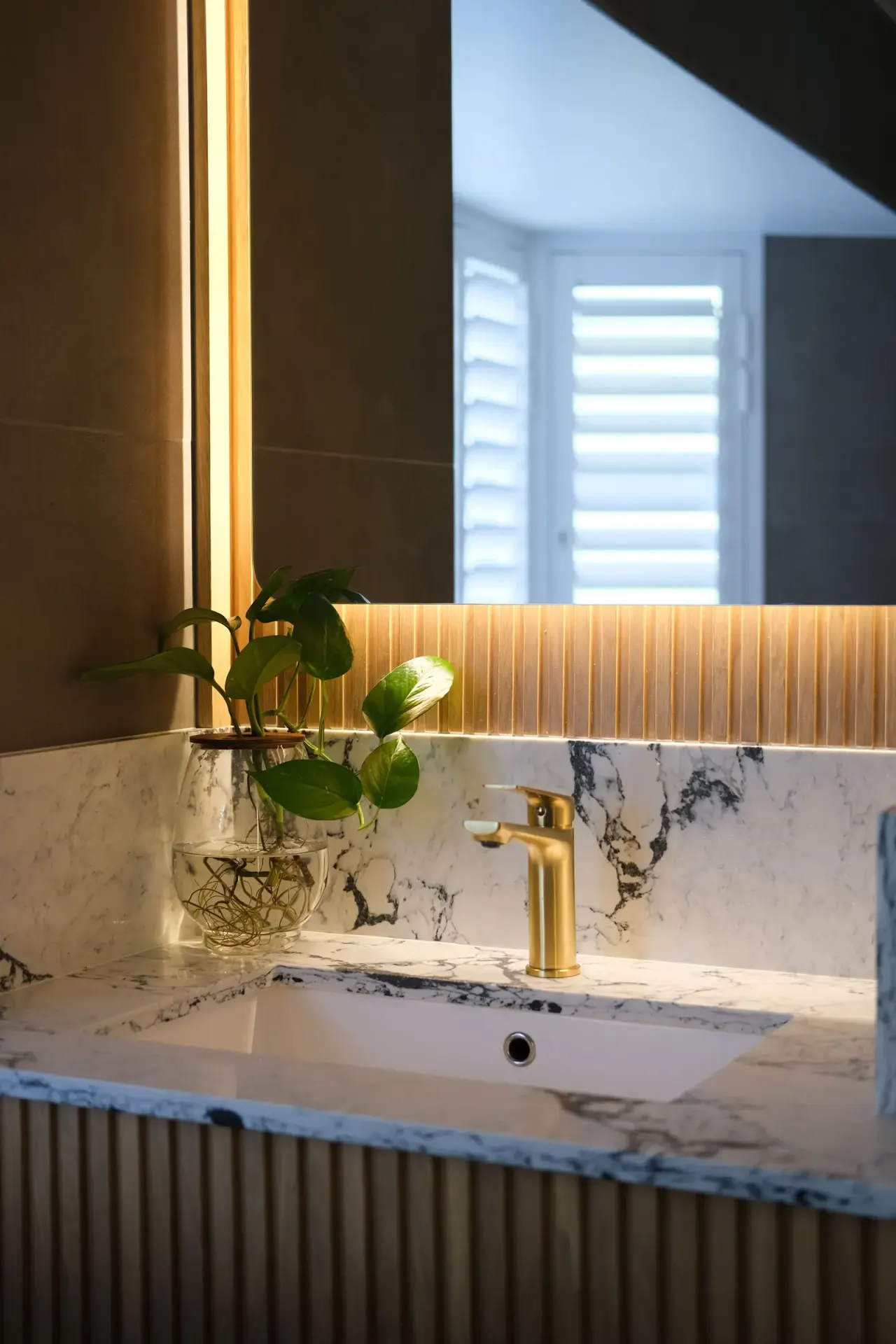 Brushed brass basin mixer on a marble vanity with a backlit mirror
