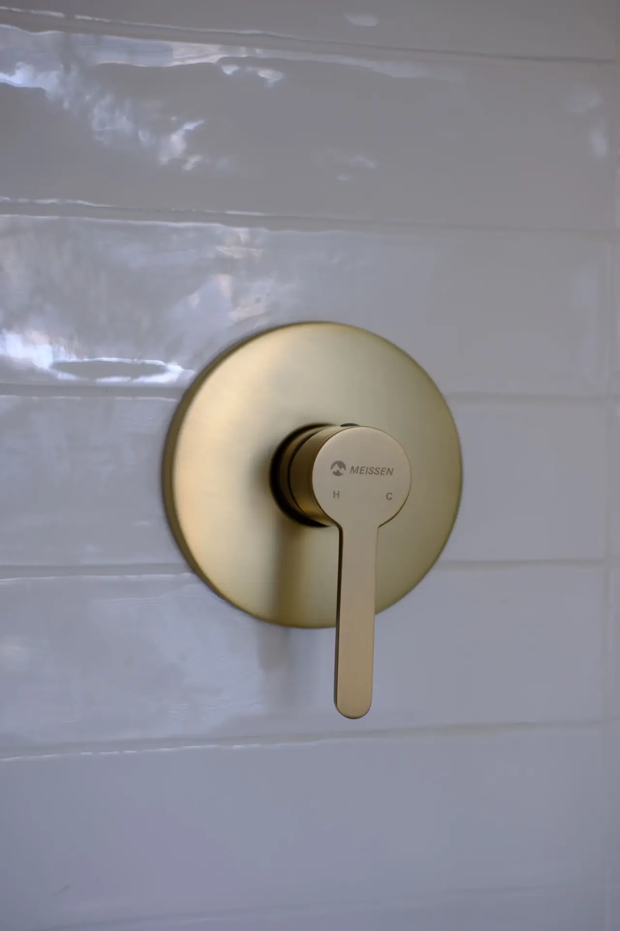 Brushed brass concealed shower mixer on a white tiled wall