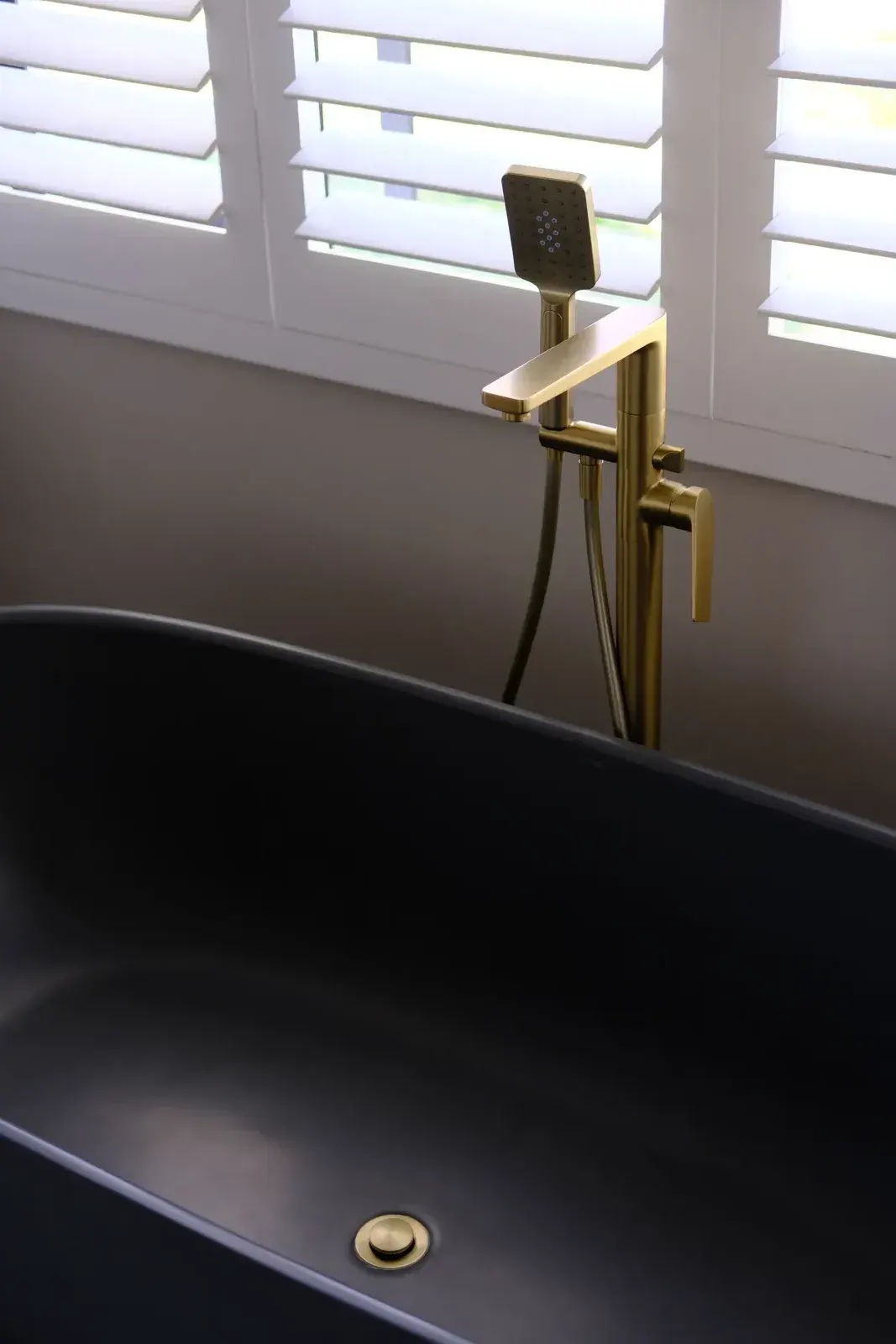 Brushed brass freestanding bath mixer with handheld shower beside a black bath