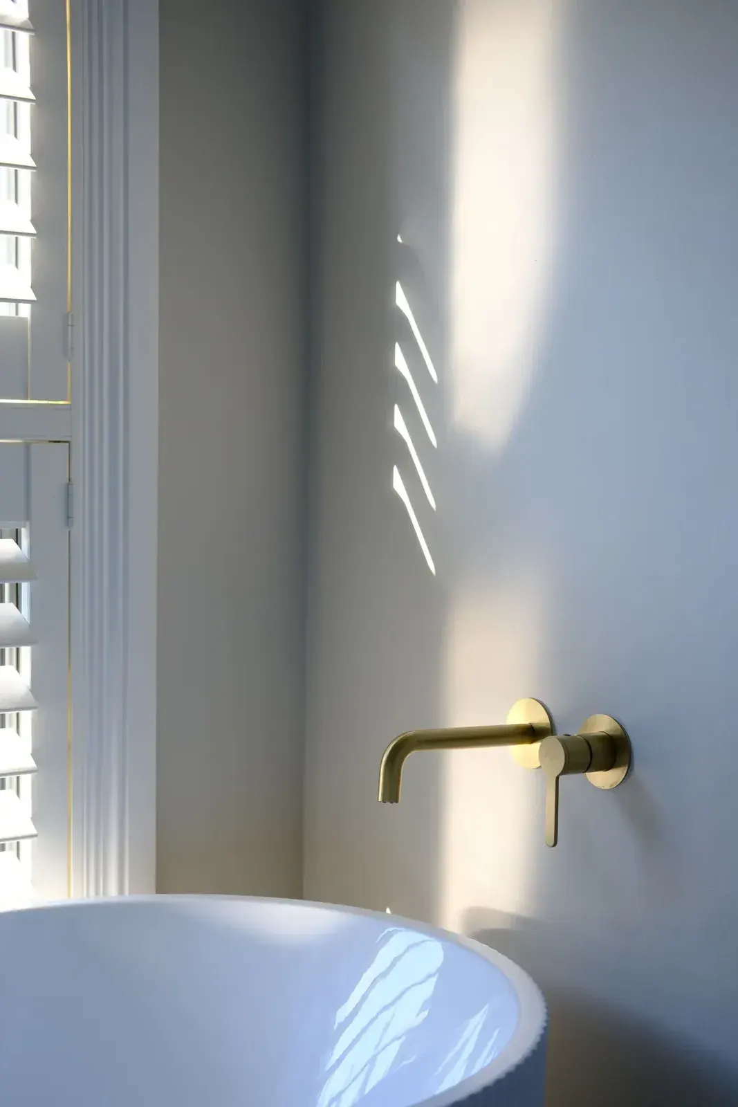 Brushed brass wall-mounted basin mixer above a vessel basin