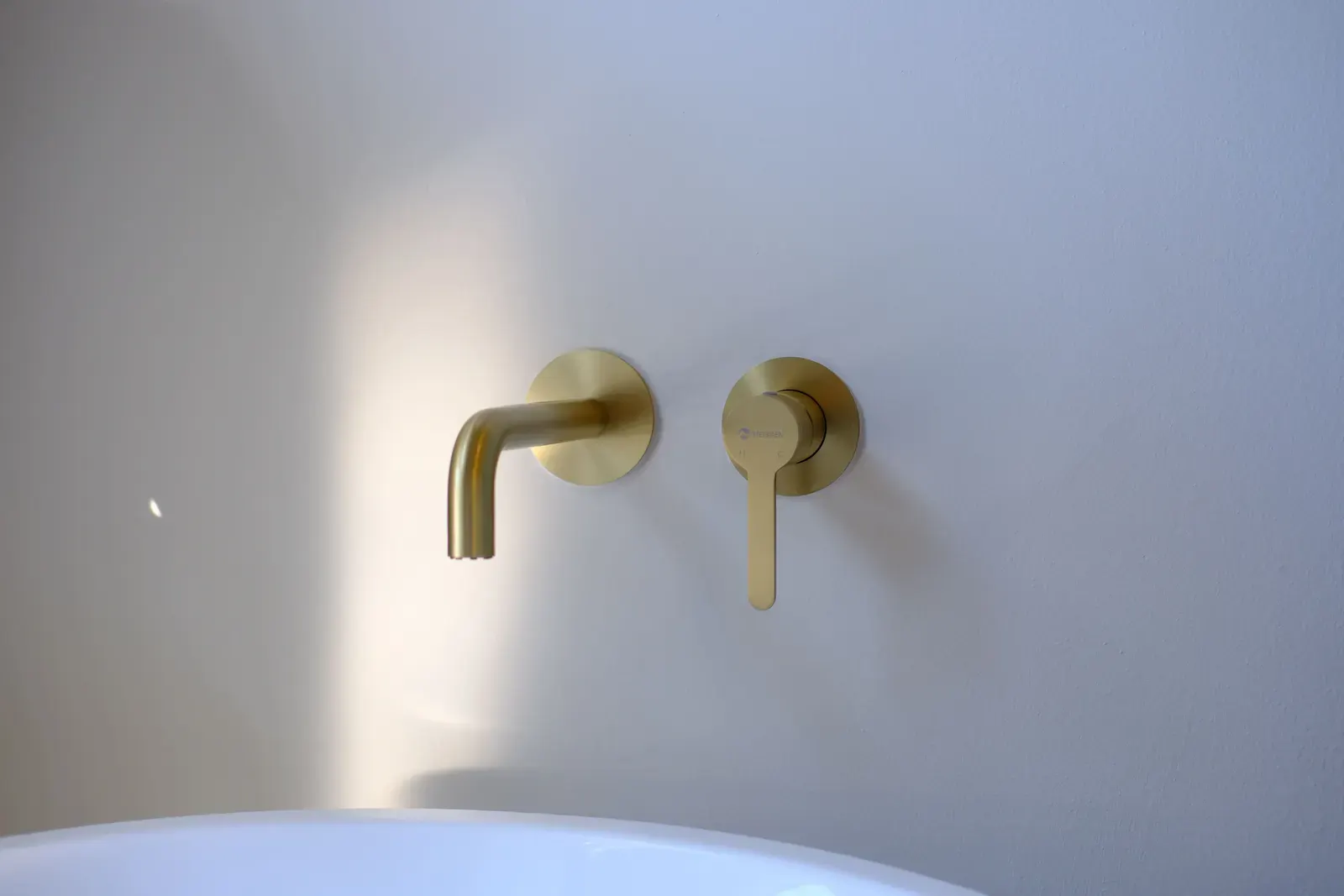 Brushed brass wall-mounted basin mixer above a freestanding bath