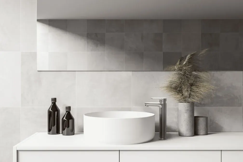 Chrome tall basin mixer beside a round white vessel basin on a minimalist grey-tiled vanity