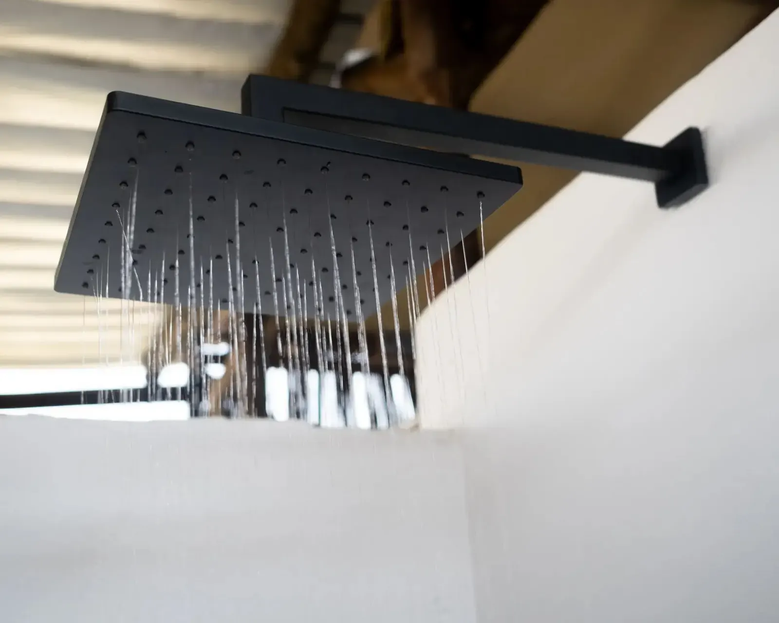Matte black square rain shower head with water flowing
