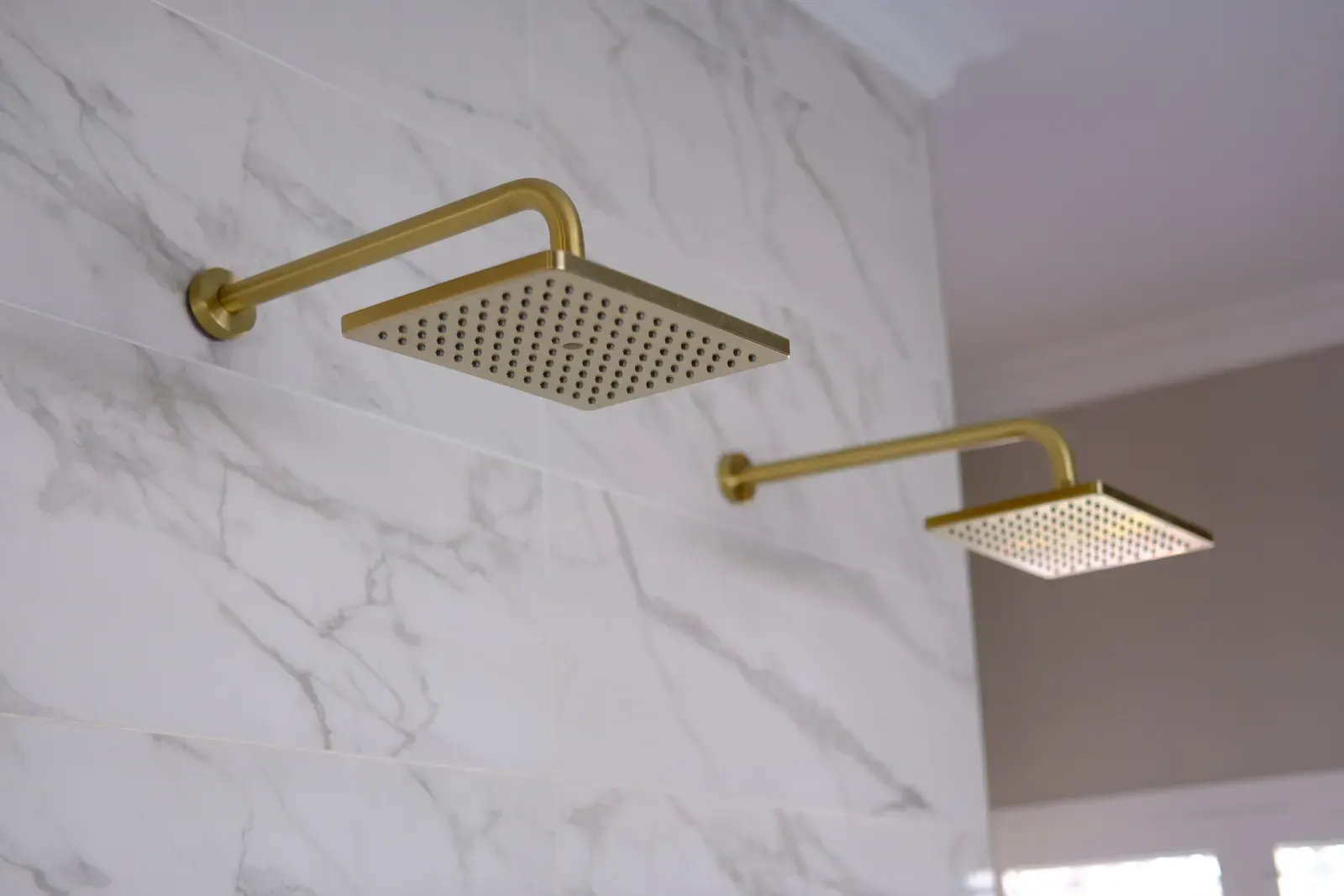 Brushed brass square rain shower heads on a marble tiled wall