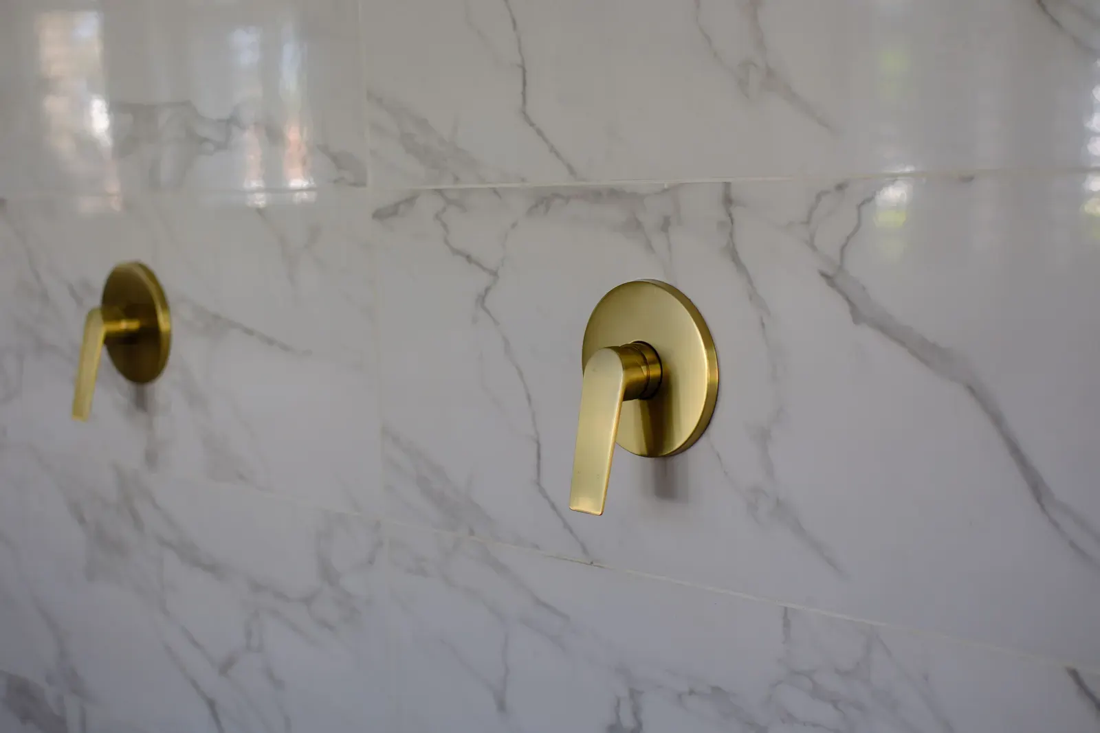 Brushed brass wall-mounted basin mixer and spout on a marble wall